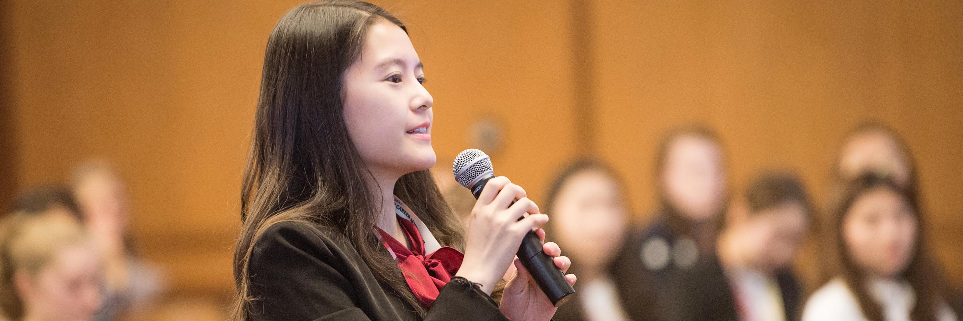 Young Asian woman holds a mic up to speak.