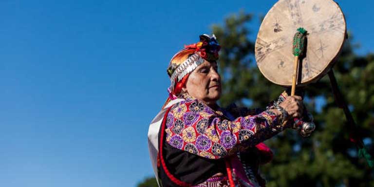 Native American person hitting drum with drum stick