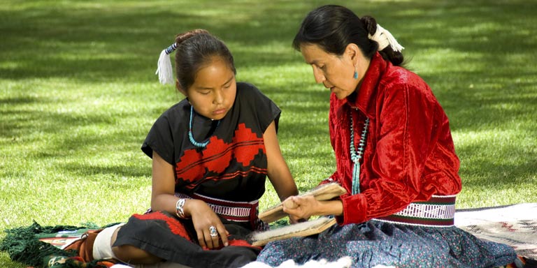 An older Navajo woman sits and talks with a young Navajo girl