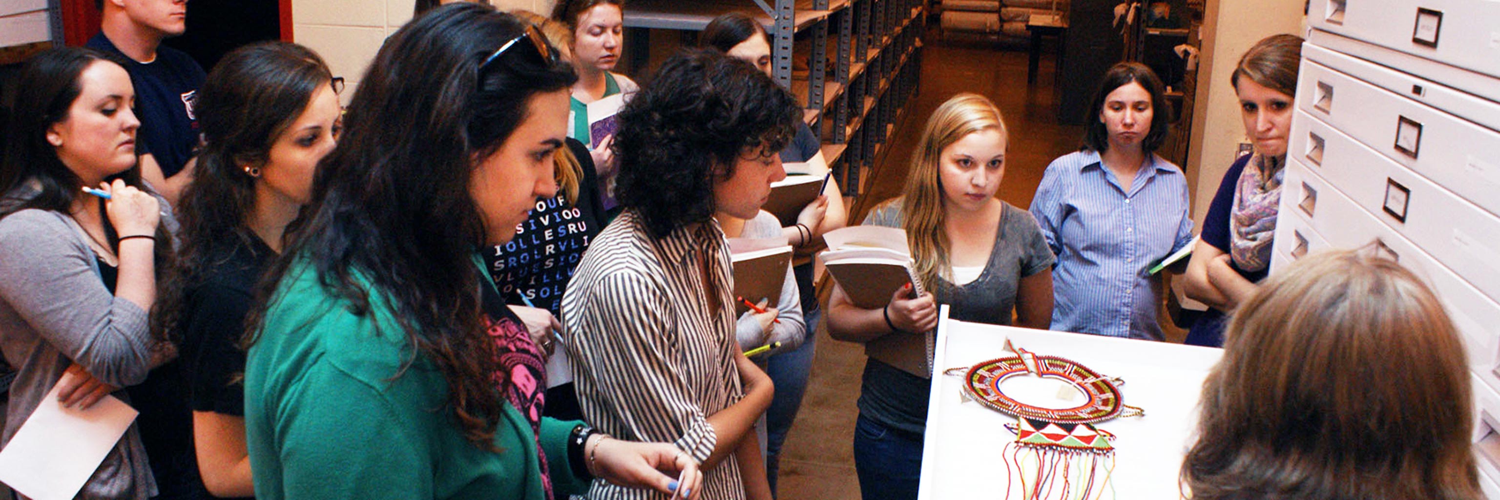 A group of students stand looking at a display and taking notes