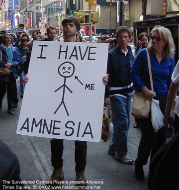 Man standing on a city street holding a sign that says, "I have amnesia"
